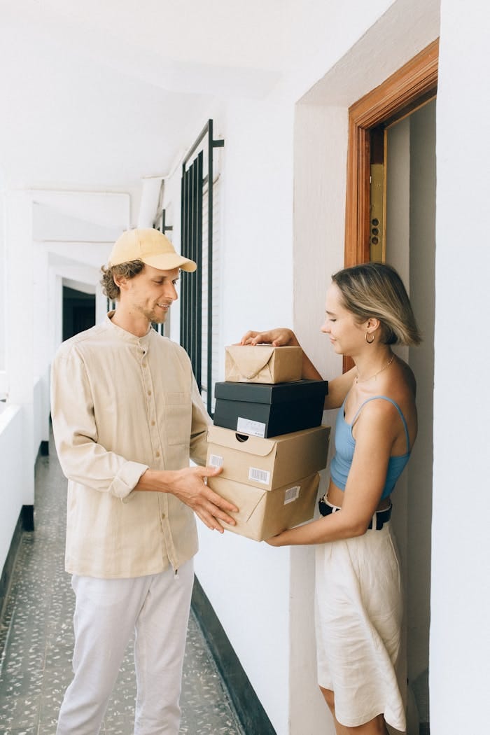 A woman receives multiple packages from a delivery man at her doorstep in a bright hallway.
